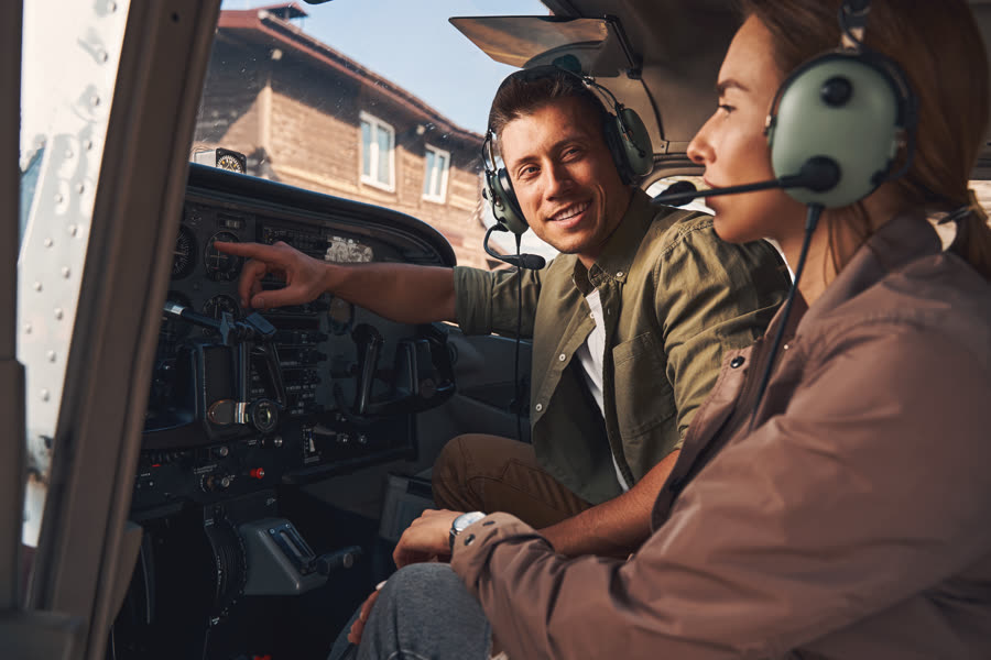 A flight instructor pointing out cockpit instruments to a student pilot wearing an aviation headset